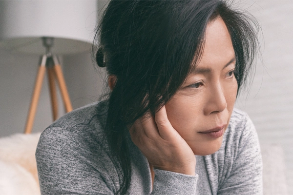 Adrenal-Fatigue-Doctor A middle-aged asian woman sitting on her couch, resting her head on her hand, suffering from adrenal fatigue. Get treatment for adrenal fatigue syndrome from Regenerative Medical Institute in Greenville.
