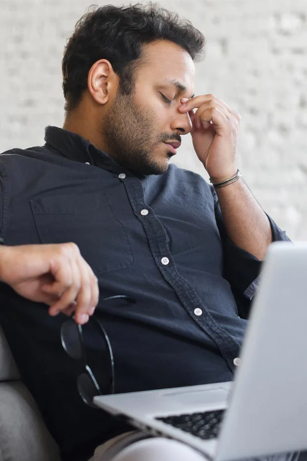 Adrenal-Fatigue-Treatment A middle-aged man with a laptop closing his eyes and rubbing his nose. He needs treatment for Adrenal Fatigue Syndrome from Regenerative Medical Institute in Greenville.