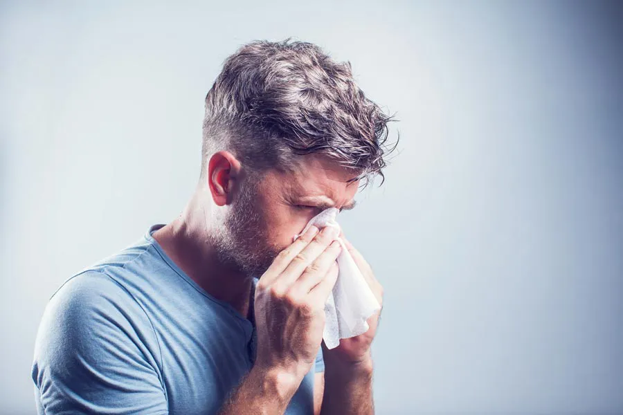 Allergies-Doctor A man in a gray shirt blows his nose. Get help for allergies from Regenerative Medical Institute in Greenville.