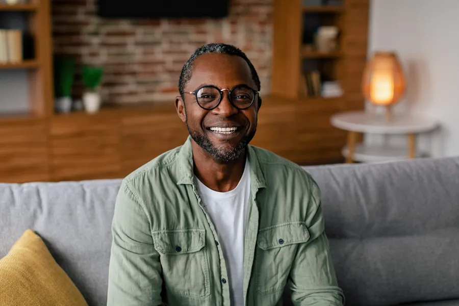 Andropause-Doctor A middle aged black man in a green button up shirt sits on his couch smiling, happy with his treatment for andropause and low testosterone from Regenerative Medical Institute in Greenville.