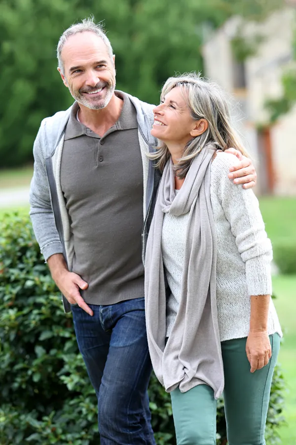 Bioidentical-Hormone-Therapy-Treatment A mature couple in gray toned clothes and jeans walk happily outside, happy with their successful bioidentical hormone treatments from Regenerative Medical Institute in Greenville.