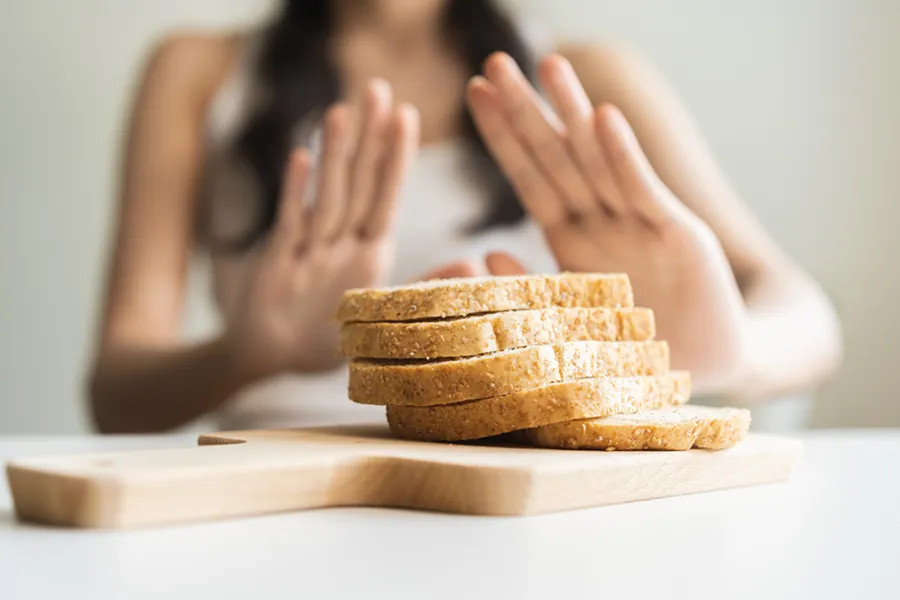 Celiac-Disease-Clinic Close up of a stack of bread slices on a cutting board with a woman's hands behind them, refusing to eat. Get treatment for Celiac Disease from Regenerative Medical Institute in Greenville.