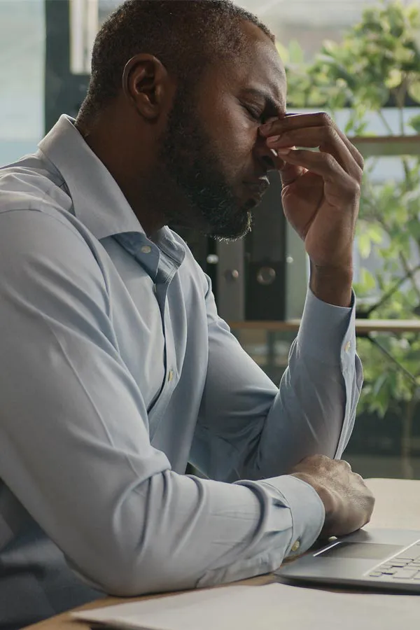 Chronic-Fatigue-Treatment A black man rubbing the top of his nose at his desk, in need of chronic fatigue treatment from Regenerative Medical Institute in Greenville.