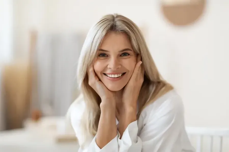 EmpowerRF-Clinicwebp A middle-aged woman with long blonde hair rests her face in her hands smiling. Get EmpowerRF vaginal rejuvenation treatment from Regenerative Medical Institute in Greenville.