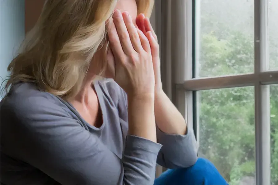 Graves-Disease-Clinic A blonde woman in a gray shirt sits in front of a window on a rainy day covering her eyes with her hands. Get treatment for Grave's Disease from Regenerative Medical Institute in Greenville.