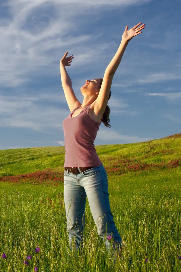 Graves-Disease-Treatment A woman in a tank top and jeans looks up with her arms outstretched to the sky in a field after successful treatment for Grave's Disease from Regenerative Medical Institute in Greenville.