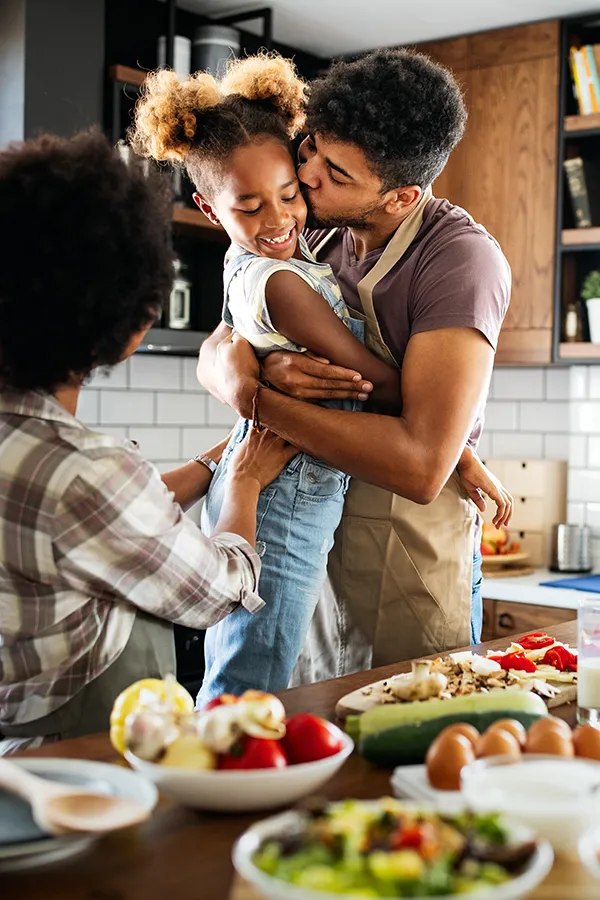 Gut-Health-Treatment A man holds his daughter and kisses her cheek as the family makes a healthy dinner in the kitchen. Get help for digestive issues and gut health from Regenerative Medical Institute in Greenville.