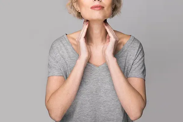 Hashimotos-Thyroiditis-Doctor An older blonde woman in a gray t-shirt holds her hands to her neck checking for signs of thyroid problems. Get help for Hashimoto's Thyroiditis from Regenerative Medical Institute in Greenville.