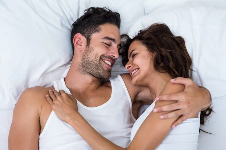 Hydromax-Pump-Clinic A brunette couple lie in bed embracing and smiling excitedly at each other. Get Hydromax Pump for penis enlargement treatment from Regenerative Medical Institute in Greenville.