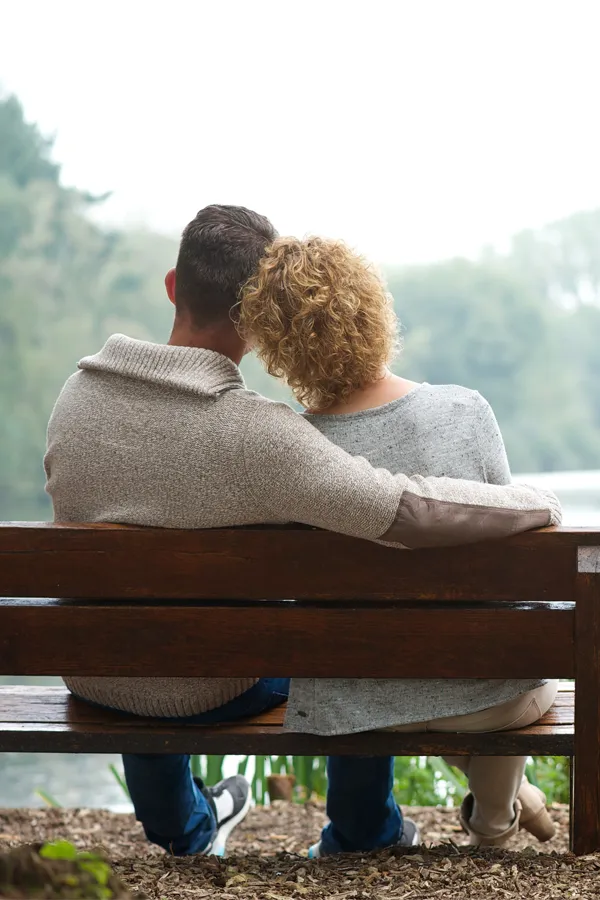 Integrative-Medicine-Treatment A man with his arm around a woman are shown from behind sitting on a bench on a serene morning. Get integrative medicine treatment from Regenerative Medical Institute in Greenville.