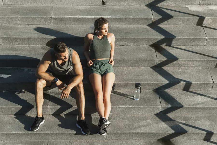 A couple in gray and green track clothes resting after a workout on stone steps, happy with their weight loss plans from Regenerative Medical Institute in Greenville.