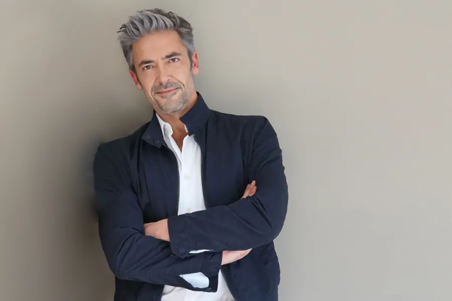 Medications-for-Erectile-Dysfunction-Clinic A handome middle-aged man in a blue jacket leans against a wall with his arms folded confidently. Get medications for erectile dysfunction from Regenerative Medical Institute in Greenville.