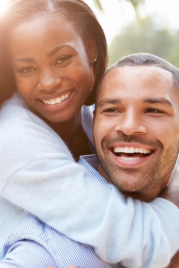 Medications-for-Erectile-Dysfunction-Treatment A happy black woman hugs her smiling husband while on piggyback. Get medications for erectile dysfunction from Regenerative Medical Institute in Greenville.