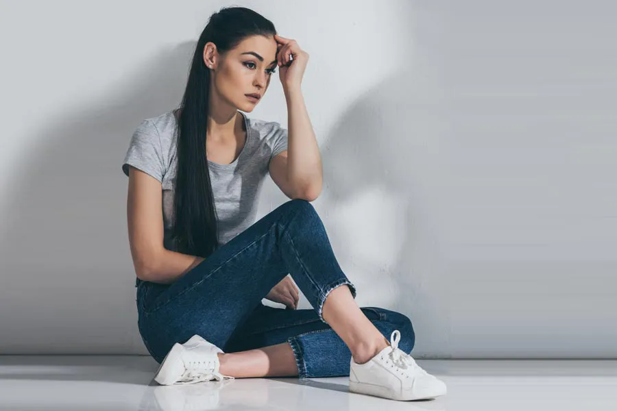 PCOS-Doctor A young brunette woman in a gray t-shirt and jeans sits against a gray wall with her head resting on her hand and a distressed expression. Get help for Polycystic Ovarian Syndrome (PCOS) from Regenerative Medical Institute in Greenville.