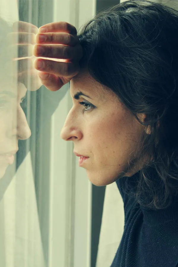 PCOS-Treatment A brunette woman in a thin dark turtleneck looks out the window with a serious expression, suffering from PCOS. Get treatment for Polycistic Ovarian Syndrome/PCOS from Regenerative Medical Institute in Greenville.