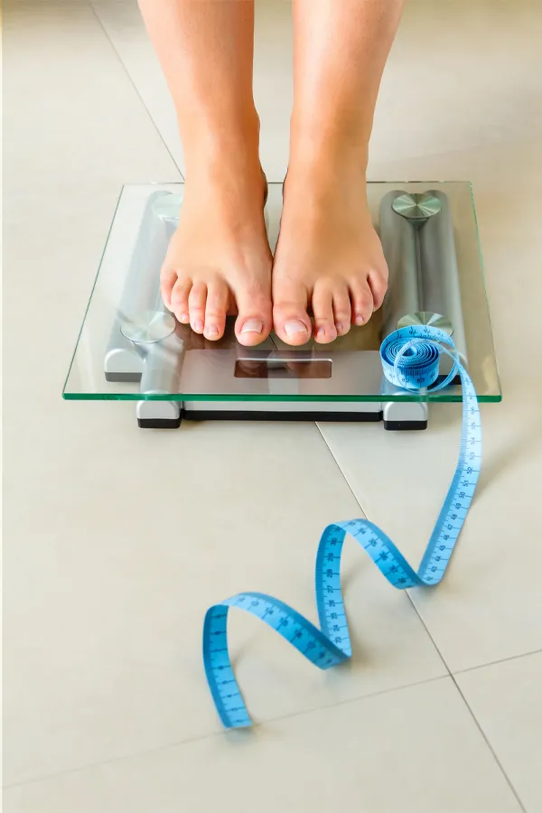 Weight-Loss-Resistance-Treatment Close-up of a woman's feet standing on a scale, with measuring tape by her toes, getting treatment for weight loss resistance from Regenerative Medical Institute in Greenville.